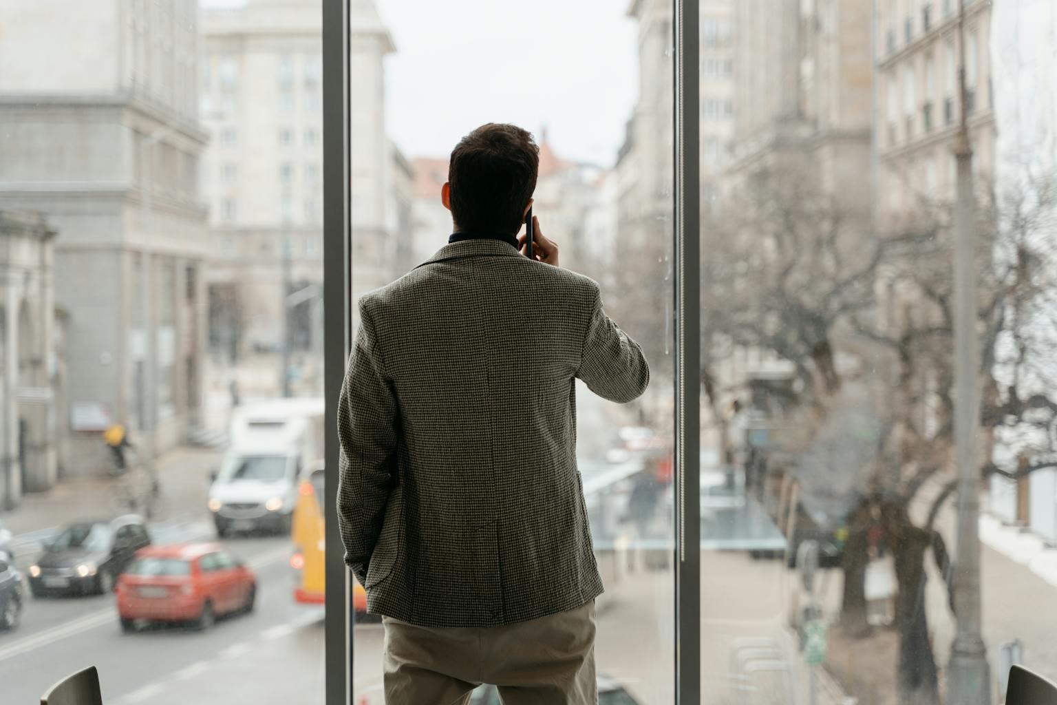 Homme en costume observant le chaos d'une grande ville à travers la fenêtre d’un bureau lumineux – Vincent, fondateur de Penser Finance